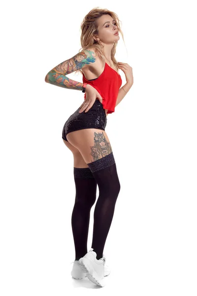 Sexy blonde twerk femme avec le corps tatoué et les cheveux longs bouclés pose en studio . — Photo