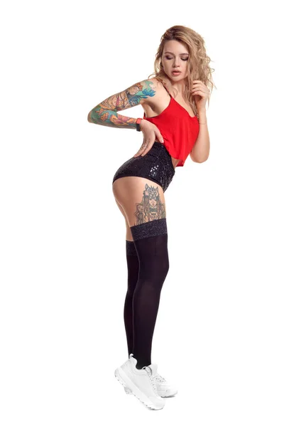 Sexy blonde twerk vrouw met tattoed lichaam en lang krullend haar is poseren in Studio. — Stockfoto