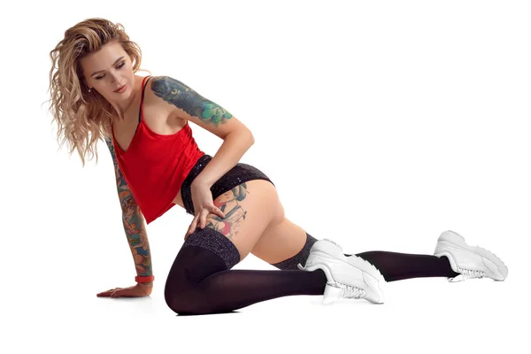 Sexy blonde twerk vrouw met tattoed lichaam en lang krullend haar is poseren in Studio. — Stockfoto