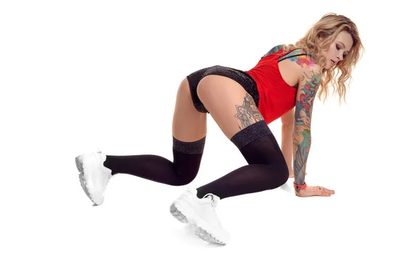 Sexy blonde twerk femme avec le corps tatoué et les cheveux longs bouclés pose en studio . — Photo