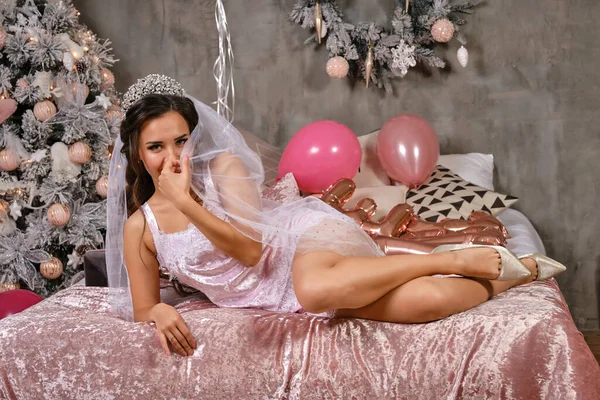 Lány szexi fény fehérnemű és fehér fátyol élvezi a tyúk-party menyasszony, feküdt az ágyon, mosolygós. Karácsonyfa, dekorációk, lufik. Közelkép. — Stock Fotó