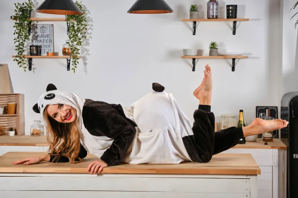 Dame habillée en pyjama en peluche sous forme de personnage de dessin animé panda s'amuse à enterrement de vie de jeune fille, posant sur la table de cuisine, souriant. Gros plan . — Photo