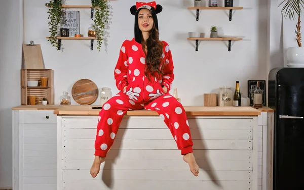 Maiden se oblékla do červeného plyšového pyžama ve formě kreslené postavičky myši. Bavit se na rozlučce se svobodou sedí na kuchyňském stole, ukazuje jazyk. — Stock fotografie