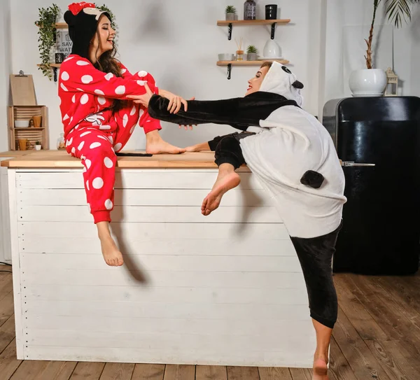 Las mujeres vestidas con pijamas de felpa en forma de personajes de dibujos animados se están divirtiendo en la despedida de soltera, subiendo a una mesa de cocina. Primer plano . —  Fotos de Stock