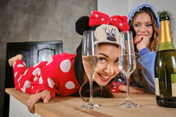 Maidens dressed in plush pajamas in form of cartoon characters enjoying bachelorette party, drinking champagne, posing on kitchen worktops. Close-up
