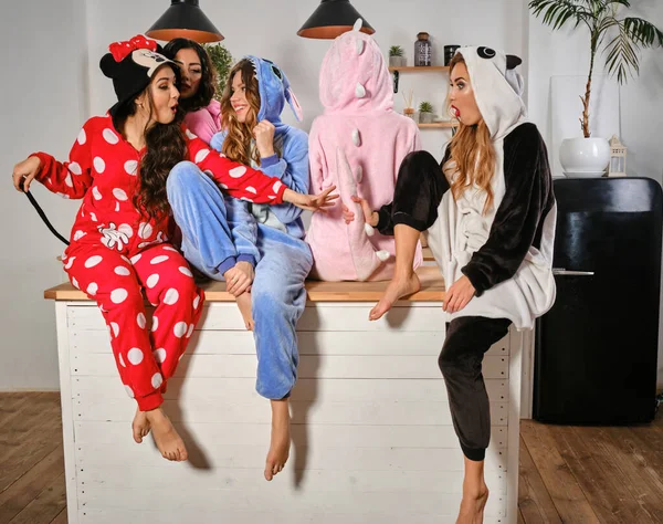 Γοητευτικές κοπέλες ντυμένες με βελούδινες πιτζάμες με τη μορφή χαρακτήρων κινουμένων σχεδίων διασκεδάζουν στο μπάτσελορ πάρτι, ποζάροντας σε τραπέζι κουζίνας. Κοντινό πλάνο. — Φωτογραφία Αρχείου