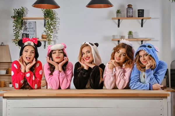 Las mujeres vestidas con pijamas de felpa en forma de personajes de dibujos animados que se divierten en la despedida de soltera, de pie detrás de la mesa de la cocina, sonriendo. Primer plano . —  Fotos de Stock