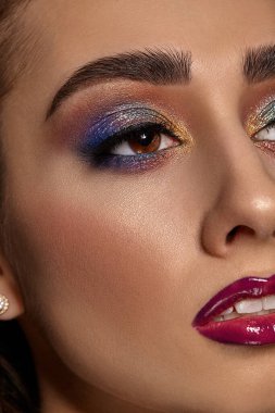 Lüks makyajlı ve mükemmel ciltli esmer kadın başka tarafa bakıyor. Mavi ve altın göz farı, uzun kirpikler, parlak bordo dudaklar ve beyaz dişler. Profesyonel maquillage. Kapat.