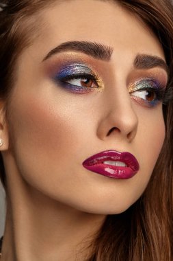 Lüks makyajlı ve mükemmel ciltli esmer kadın yan bakıyor. Çok renkli göz farı, takma kirpikler, parlak bordo dudaklar. Profesyonel maquillage. Kapat.