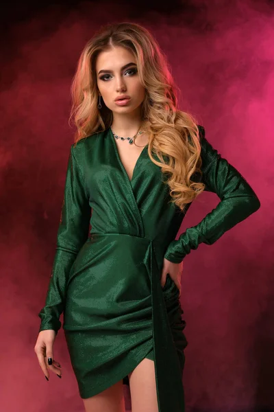 Mujer rizada rubia en vestido elegante verde y joyas. Ella ha puesto su mano en la cintura, posando sobre un colorido fondo ahumado. Moda, belleza. De cerca. — Foto de Stock