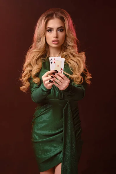 Ξανθιά σγουρή κοπέλα σε πράσινο κομψό φόρεμα και κοσμήματα. Δείχνει δύο τραπουλόχαρτα, να ποζάρουν σε καφέ φόντο. Πόκερ, καζίνο. Κοντινό πλάνο — Φωτογραφία Αρχείου