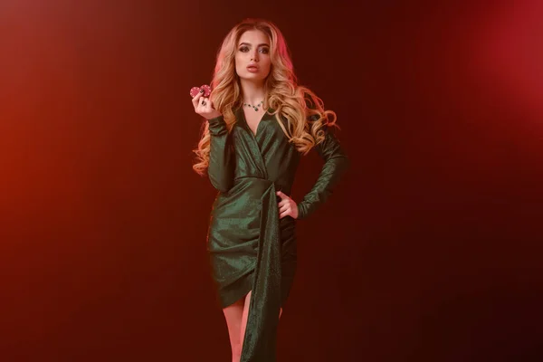 Donna bionda con trucco brillante, in abito elegante verde e gioielli. Mostrando due chip rossi, in posa su sfondo colorato con retroilluminazione. Primo piano — Foto Stock