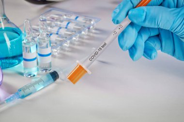 Elleri mavi, tek kullanımlık eldivenlerle test seti tutuyor. Renkli kimyasal reaksiyonlu tıbbi mataralar. Sıvı ve şırıngalı ampuller beyaza izole edilmiş. Coronavirus 'un laboratuvar araştırması. Sınavı kapat