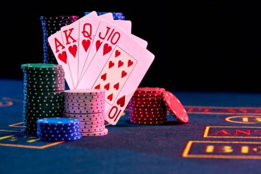 Pokerde kazanan kombinasyon renkli çiplere yaslanarak oyun masasının mavi kapağında duruyor. Siyah arka plan. Kumar eğlencesi, iskambil kartları, kumarhane konsepti. Yakın çekim..