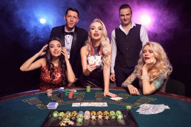 Genç ve yakışıklı sınıf arkadaşları kumarhanede poker oynuyorlar. Gençler büyük bir galibiyet için bahis oynuyorlar. Siyah duman arka planında kırmızı ve mavi arka farlara karşı masada poz veren kameraya bakıyorlar. Kartlar, çipler, para, ga