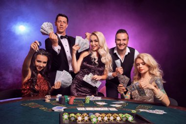 Bir grup mutlu genç arkadaş kumarhanede poker oynuyorlar. Gençler büyük bir galibiyet için bahis oynuyorlar. Gülümsüyorlar ve masada siyah duman arka planında kırmızı ve mavi arka farlara karşı biraz para tutuyorlar. Kartlar, fişler, para, gam