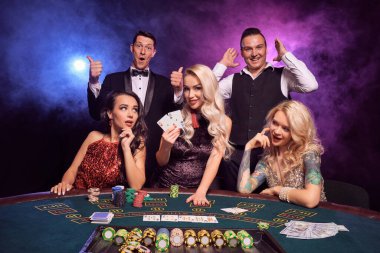 Bir grup genç pozitif yoldaş kumarhanede poker oynuyor. Gençler büyük bir galibiyet için bahis oynuyorlar. Gülümsüyorlar ve masada siyah dumanlı kırmızı ve mavi arka farlara karşı poz veren iki as gösteriyorlar. Kartlar, çipler, para,