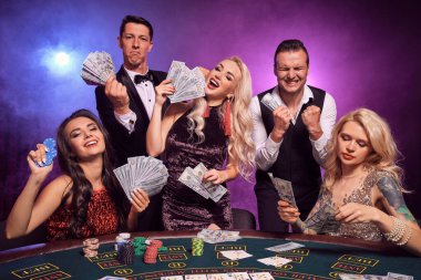 Bir grup zengin genç kumarhanede poker oynuyor. Gençler büyük bir galibiyet için bahis oynuyorlar. Gülümsüyorlar ve masada siyah duman arka planında kırmızı ve mavi arka farlara karşı biraz para tutuyorlar. Kartlar, çipler, para, g