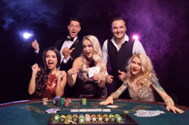 Bir grup komik genç kumarhanede poker oynuyor. Gençler büyük bir galibiyet için bahis oynuyorlar. Gülümsüyorlar ve siyah dumanlı arka plandaki kırmızı ve mavi ışıklara karşı masada poz veren kameraya bakıyorlar. Kartlar, çipler, para, 