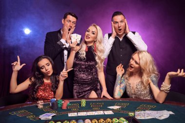Genç ve mutlu bir grup kumarhanede poker oynuyor. Gençler büyük bir galibiyet için bahis oynuyorlar. Gülümsüyorlar ve masada siyah dumanlı kırmızı ve mavi arka farlara karşı poz veren iki as gösteriyorlar. Kartlar, çipler, para, ga