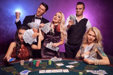 Bir grup zengin genç arkadaş kumarhanede poker oynuyorlar. Gençler büyük bir galibiyet için bahis oynuyorlar. Gülümsüyorlar ve masada siyah duman arka planında kırmızı ve mavi arka farlara karşı biraz para tutuyorlar. Kartlar, çipler, para, g