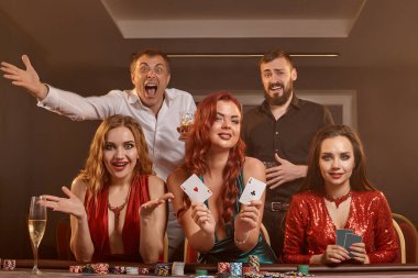 Mutlu arkadaşlar kumarhanede poker oynuyorlar. Kazanmalarını kutluyorlar, gülümsüyorlar ve karanlık bir duman geçmişine karşı masada poz veriyorlar. Kartlar, fişler, para, alkol, servet, kumar, eğlence konsepti.