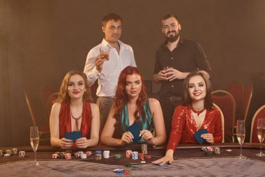 Konsantre arkadaşlar kumarhanede poker oynuyorlar. Altın gençler büyük bir galibiyet için iddiaya girerken masada koyu bir duman arka planına karşı poz veriyorlar. Kartlar, çipler, para, servet, alkol, kumar, eğlence konsepti.