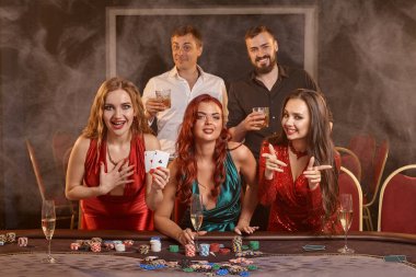 Şanslı meslektaşlarım kumarhanede poker oynuyorlar. Kazanmalarını kutluyorlar, gülümsüyorlar ve karanlık bir duman geçmişine karşı masada poz veriyorlar. Kartlar, çipler, para, alkol, kumar, eğlence konsepti.