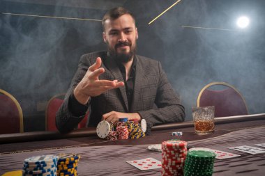 Klasik gri takım elbiseli yakışıklı sakallı adam kumarhanede poker oynuyor. Masada elinde kartlar ve bir bardak viskiyle oturuyor. Masaya iki kumar fişi fırlatıyor, gülümsüyor ve onlara bakıyor. Kumar bağımlılığı. Samimi.