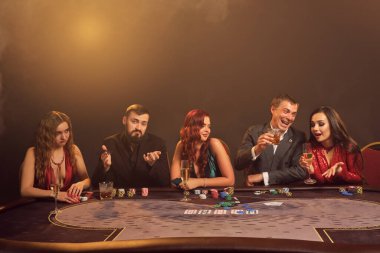 Mutlu ortaklar kumarhanede poker oynuyor. Büyük bir galibiyet için iddiaya giriyorlar. Masada karanlık bir dumanla poz verirken. Spot ışığının altında. Kartlar, çipler, para, alkol, kumar, eğlence konsepti.
