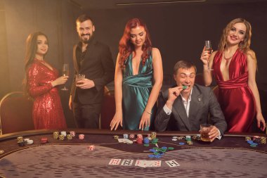 Neşeli arkadaşlar kumarhanede poker oynuyorlar. Zaferlerini kutluyorlar, gülümsüyorlar ve çok heyecanlı görünüyorlar. Bir sahne ışığı altında, karanlık bir duman arka planına karşı poz veriyorlar. Kartlar, fişler, para, alkol, kumar, eğlence konseyi