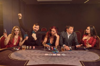 Mutlu sınıf arkadaşları kumarhanede poker oynuyorlar. Büyük bir galibiyet için iddiaya giriyorlar. Masada karanlık bir dumanla poz verirken. Spot ışığının altında. Kartlar, çipler, para, alkol, kumar, eğlence konsepti.