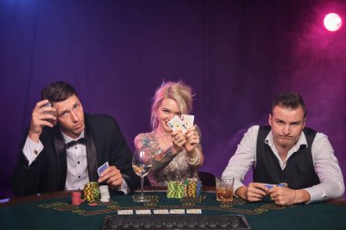 İki görkemli erkek ve güzel kadın kumarhanede poker oynuyorlar. Gençler büyük bir galibiyet için bahis oynuyorlar. Gülümsüyorlar ve masada oturan kameraya bakıyorlar. Siyah dumanlı kırmızı ve mavi bir arka fonda oturuyorlar. Kartlar, çipler, para