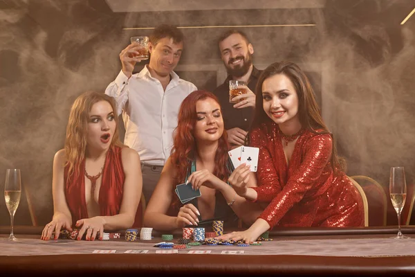 快乐的同伴们在赌场打扑克 他们正在庆祝他们的胜利 微笑着 并在黑暗的烟幕下摆出姿势坐在桌旁 娱乐概念 — 图库照片