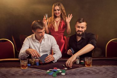 İki eski dost ve çekici bayan kumarhanede poker oynuyorlar. Büyük bir galibiyet için iddiaya giriyorlar ve masada arka plandaki sarı ışığa karşı poz verirken iyi vakit geçiriyorlar. Kartlar, çipler, para, kumar, eğlence 