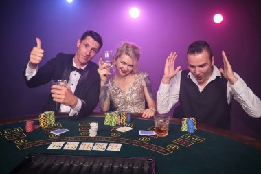 İki yakışıklı erkek ve inanılmaz kadın kumarhanede poker oynuyorlar. Gençler büyük bir galibiyet için bahis oynuyorlar. Gülümsüyorlar ve siyah duman arka planında kırmızı ve mavi bir arka lambaya karşı masaya oturarak uluyorlar. Kartlar, çipler...