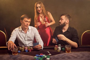 İki eski arkadaş ve çekici kız kumarhanede poker oynuyorlar. Büyük bir galibiyet için iddiaya giriyorlar, ama biraz şaşırmış görünüyorlar. Arka planda sarı bir ışığa karşı poz veriyorlar. Kartlar, fişler, para, kumar, ent