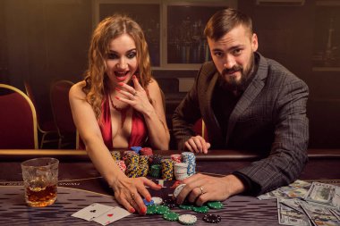 Yakışıklı zengin arkadaşlar kumarhanede poker oynuyorlar. Gençler gülümsüyor, kameraya bakıyor ve masada sigara dumanına karşı poz verirken zaferlerine seviniyorlar. Kartlar, çipler, para, kumar, eğlence konsepti.