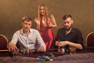 İki eski arkadaş ve çekici kadın kumarhanede poker oynuyorlar. Büyük bir galibiyet için iddiaya giriyorlar ve biraz hayal kırıklığına uğramış görünüyorlar. Masada arka plandaki sarı ışığa karşı poz veriyorlar. Kartlar, fişler, para, kumar