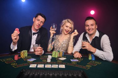 İki yakışıklı adam ve muhteşem bakire kumarhanede poker oynuyorlar. Gençler büyük bir galibiyet için bahis oynuyorlar. Gülümsüyorlar ve masada oturan kameraya bakıyorlar. Siyah dumanlı kırmızı ve mavi bir arka fonda oturuyorlar. Kartlar, çip