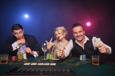 İki atletik erkek ve çekici kız kumarhanede poker oynuyorlar. Gençler büyük bir galibiyet için bahis oynuyorlar. Gülümsüyorlar ve masada oturan kameraya bakıyorlar. Siyah dumanlı kırmızı ve mavi bir arka fonda oturuyorlar. Kartlar, çipler...