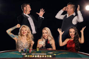 Mutlu arkadaşlar kumarhanede poker oynuyorlar. Galibiyetlerini kutluyorlar, seviniyorlar, gülümsüyorlar ve çok heyecanlı görünüyorlar. Masada beyaz bir ışığın altında karanlık bir arkaplanda poz verirken. Kartlar, fişler, para, alkol, kumar, eğlence