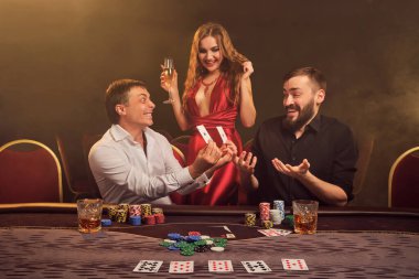 İki atletik arkadaş ve çekici bakire kumarhanede poker oynuyorlar. Zaferlerini kutluyorlar ve kazanan kombinasyonu birbirlerine gösterirken aynı zamanda sarı bir arka fonda dumanlı arka planda poz veriyorlar. Kartlar, çipler, para, kumar