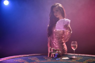 Mükemmel saç stili ve parlak makyajlı esmer kız elinde 100 dolarlık banknotlarla poz veriyor. Kumarhane, poker.