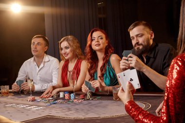 Hevesli yoldaşlar kumarhanede poker oynuyorlar. Gençler büyük bir galibiyet için iddiaya girerken masada siyah bir dumanla beyaz bir spot ışığına karşı poz veriyorlar. Kartlar, çipler, para, alkol, kumar, eğlence konsepti.