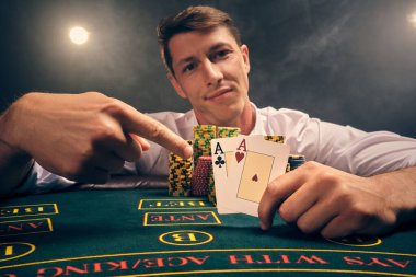 Beyaz gömlekli zeki bir adamın yakın plan çekimi, kumarhanedeki masada beyaz bir spot ışığına karşı duman içinde poker oynamaktır. Zaferini sevinçle elinde iki as ile kutluyor. Kumar bağımlılığı. Samimi duygular ve eğlence.