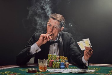 Siyah takım elbiseli ve beyaz gömlekli yakışıklı adam kumarhanenin masasında beyaz bir spot ışığına karşı duman içinde poker oynuyor. Elindeki iki ası göstererek zaferine seviniyor, puro içiyor ve başka tarafa bakıyor. Kumar bağımlısı.