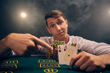 Beyaz gömlekli zeki bir insanın yakın plan çekimi, kumarhanedeki masada beyaz bir spot ışığına karşı duman içinde poker oynamaktır. Elindeki iki ası göstererek zaferine seviniyor. Kumar bağımlılığı. Samimi duygular ve eğlence anlayışı