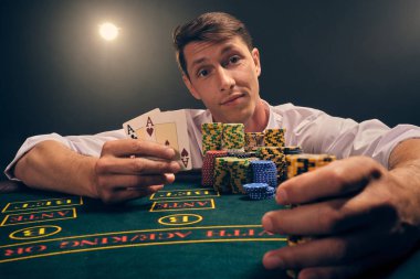 Beyaz gömlekli zeki bir erkeğin yakın plan çekimi, kumarhanedeki masada beyaz bir spot ışığına karşı duman içinde poker oynamaktır. Zaferine sevinçle seviniyor. Elinde iki as ve birkaç fiş var. Kumar bağımlılığı. Samimi duygular ve girişim