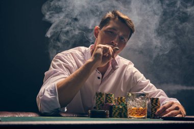 Beyaz gömlekli yakışıklı kumarhanenin masasında beyaz spot ışıklarına karşı poker oynuyor. Zaferine seviniyor ve puro içiyor. Kumar bağımlılığı. Samimi duygular ve eğlence konsepti.